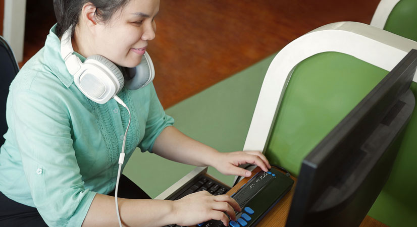 Smiling blind woman sitting in a green computer booth using a specialist keyboard
